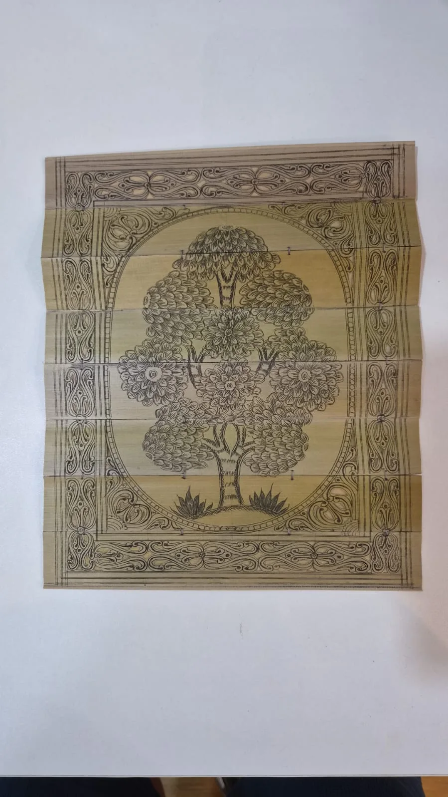 Tree and floral motifs engraved across joined palm leaves